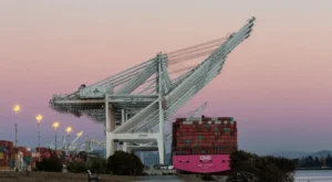 Sunset sky in background, overhead gantry cranes at a sea freight port with container ship alongside quay